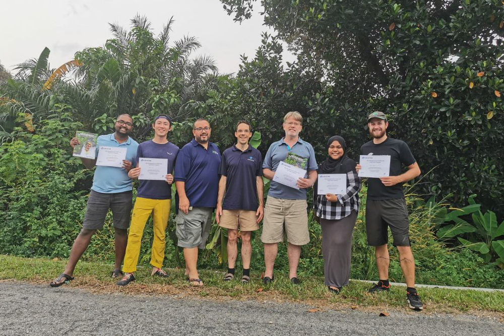 A picture of the x3si team standing next to each other on the side of a road. Some of them are holding up pieces of paper with indiscernible information on them