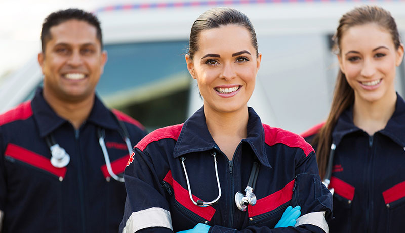 A picture of three medical personnel standing looking at the camera. There is a ambulance in the background.