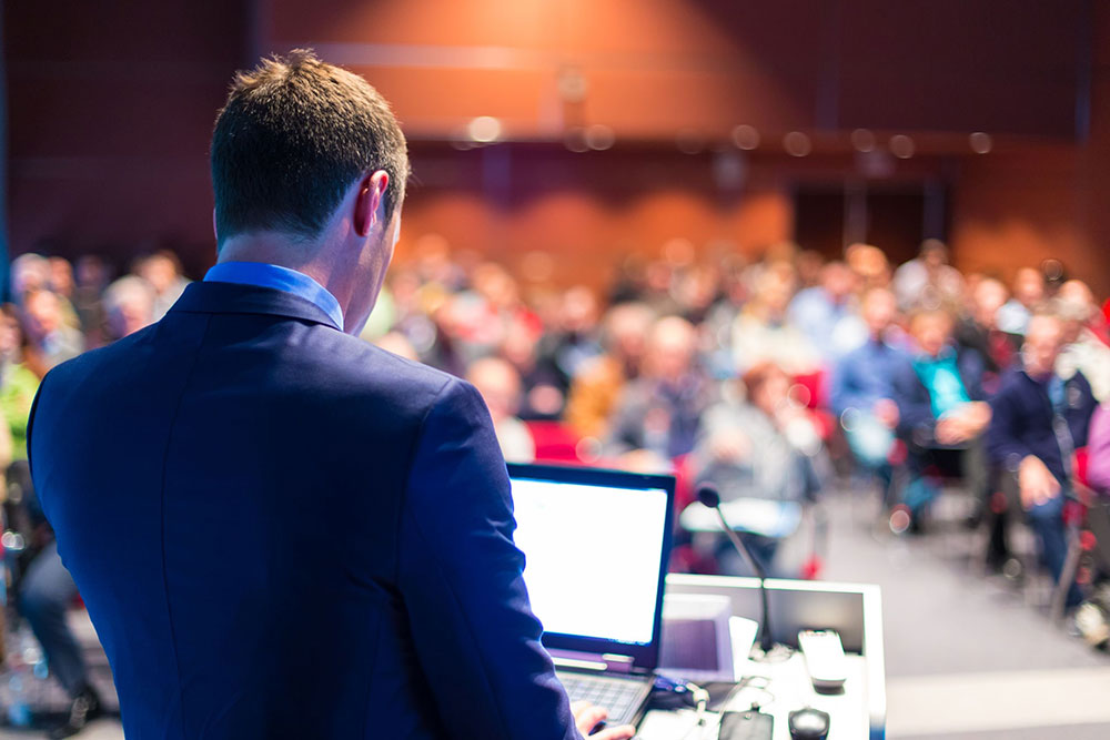 A picture of a man on his computer. There is a crowd of people in the background.